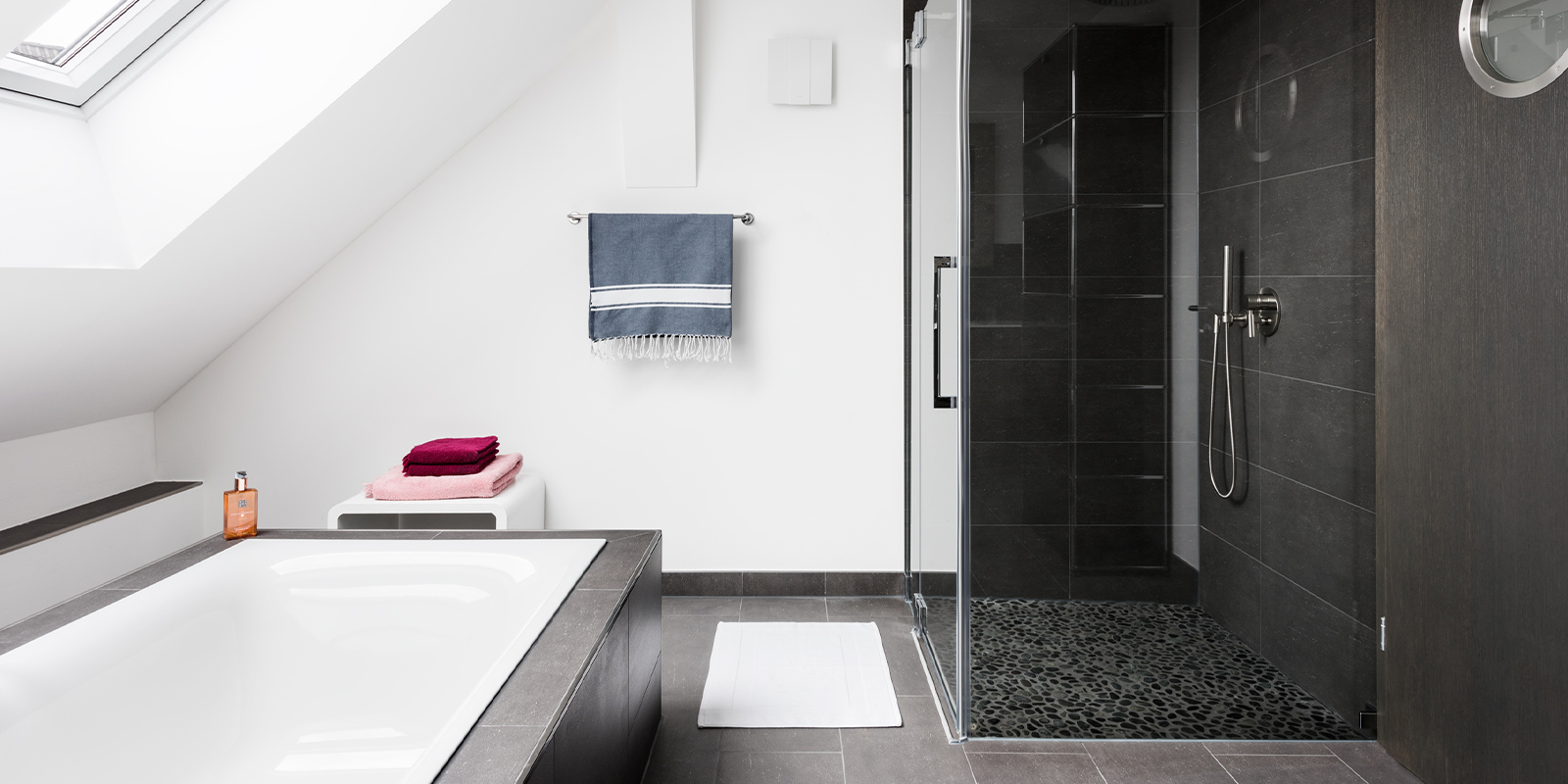 Ein modernes Badezimmer mit einer freistehenden Badewanne und einer eleganten Dusche, die mit dunklen Fliesen gestaltet ist.