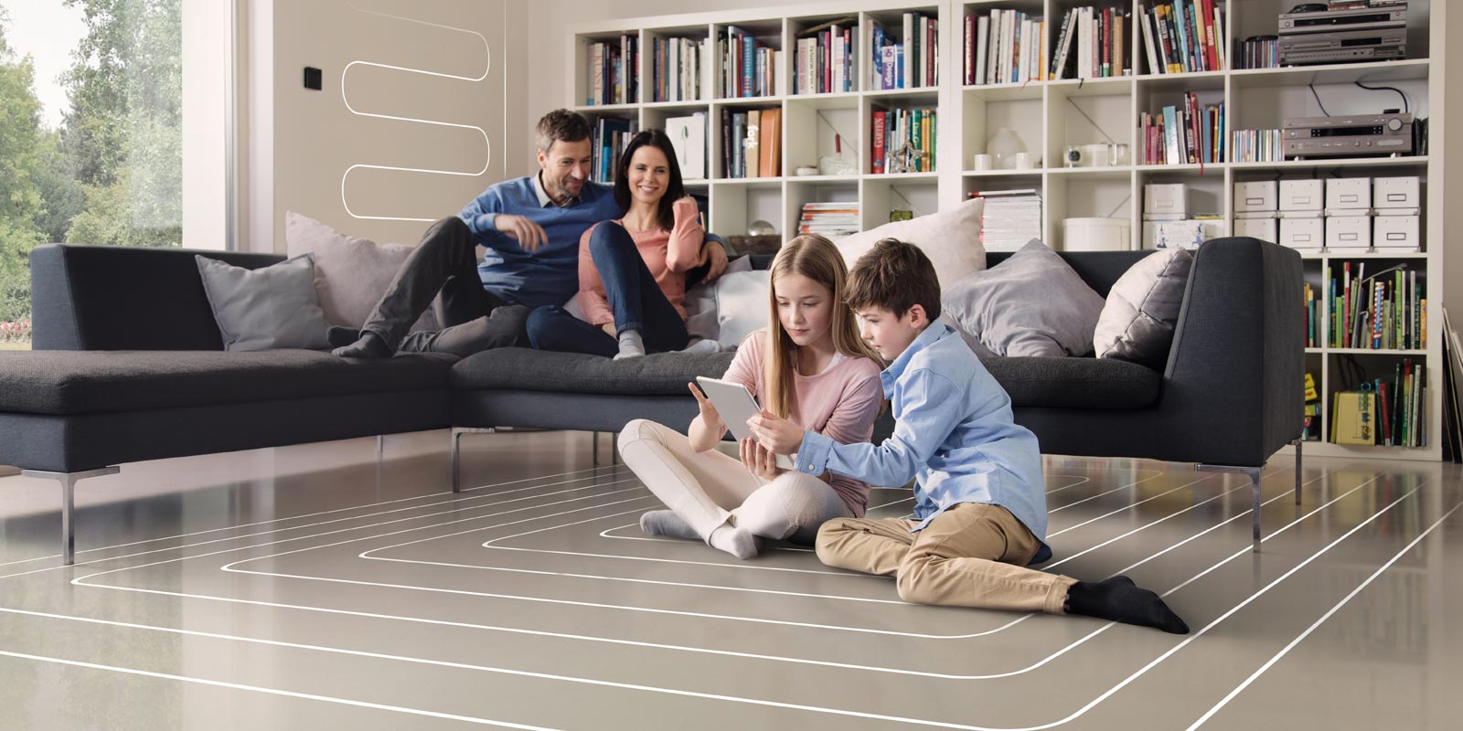 Eine Familie sitzt in einem Wohnzimmer mit einer Flaechenheizung, die beiden Kinder sitzten auf dem Boden