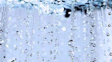 Faszinierende Tropfen, die im Licht funkeln Wassertropfen fallen in einer sanften Bewegung, während sie im Licht funkeln und eine ruhige Atmosphäre schaffen.