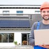 Ein Mann in Arbeitskleidung vor einer Photovoltaikanlage mit einem Laptop in der Hand