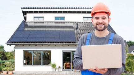 Ein Mann in Arbeitskleidung vor einer Photovoltaikanlage mit einem Laptop in der Hand