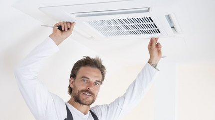 Handwerker installiert eine Klimaanlage an der Decke Ein Mann mit Vollbart hält ein Lüftungsgitter an der Decke