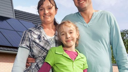 Eine kleine Familie, im Hintergrund ist ein Haus mit einer Photovoltaikanlage