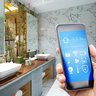 Ein modernes Badezimmer mit eleganten Waschbecken und einem Smartphone, das eine smarte Steuerung zeigt.