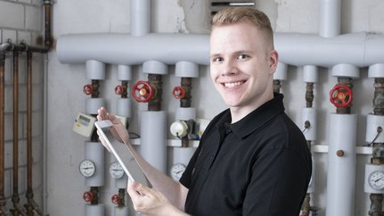 Ein Anlagenmechaniker vor einer Heizungsanlage mit einem Tablet