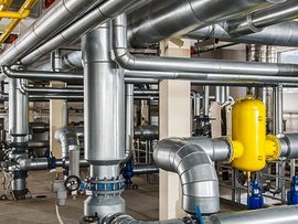 Komplexes Rohrleitungssystem in einer industriellen Umgebung Ein Raum mit einer Edelstahl Rohranlage, Pumpen und Kompressoren.